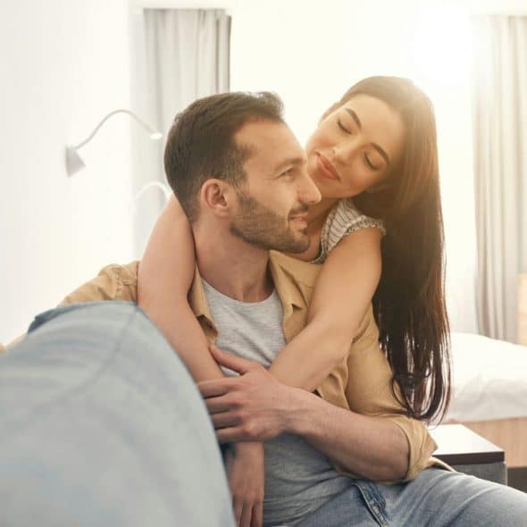A happy couple embraces on a couch, bathed in warm sunlight.