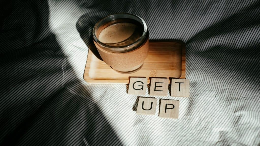 Wooden letters spelling out “get up” beside a glass of coffee