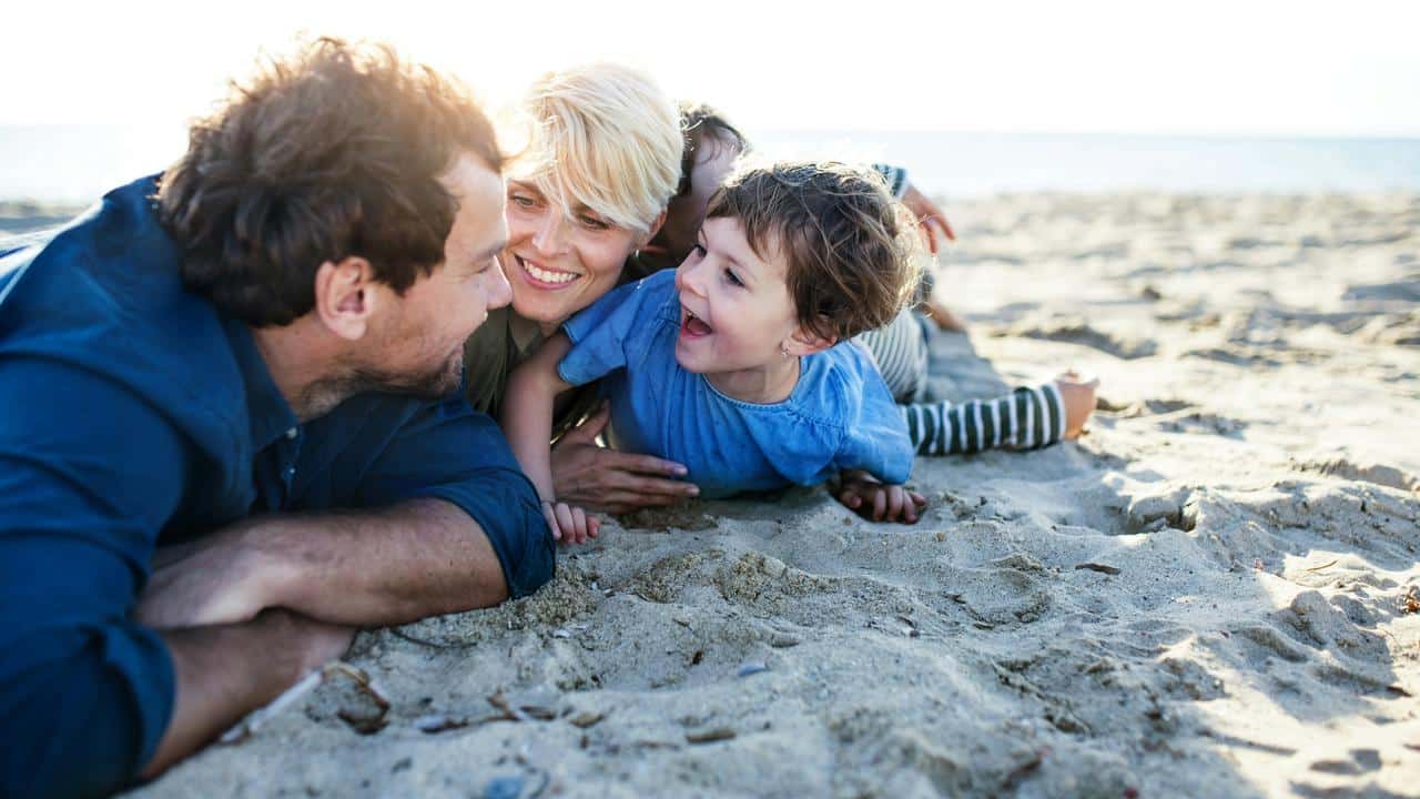 A family of three lying on a sandy beach, smiling together.