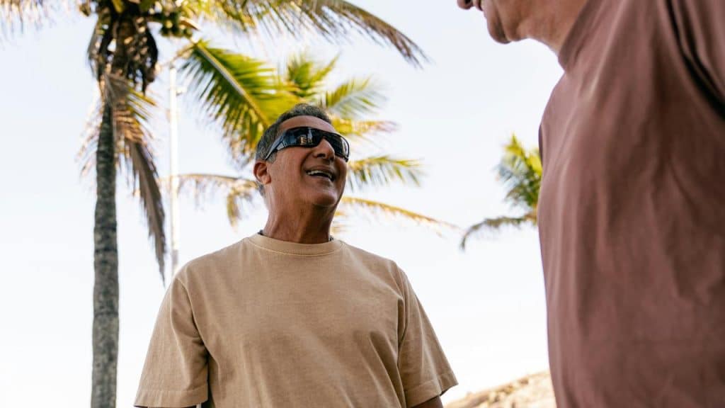 A man in sunglasses smiling outdoors near palm trees.