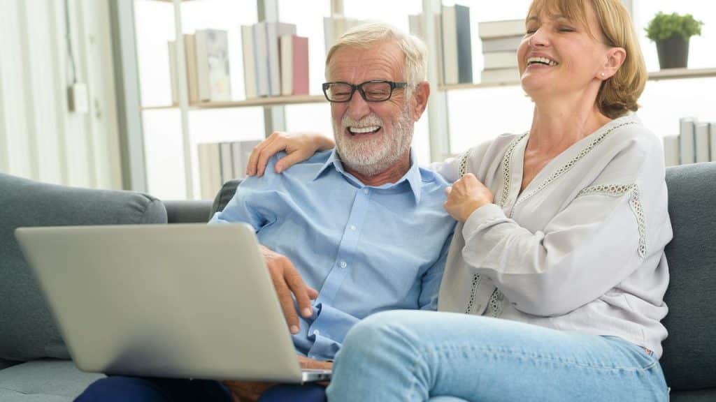 An older couple laughing together at a laptop.