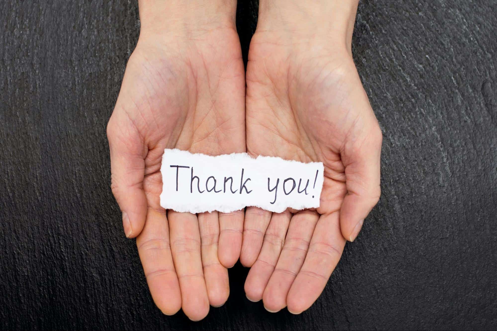 A person with a paper on his hand saying “thank you”.