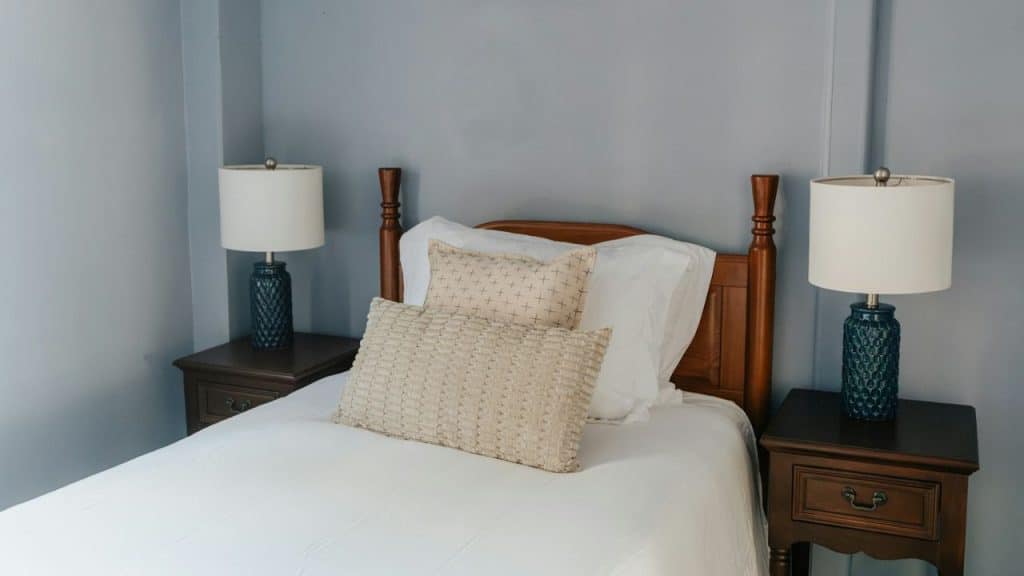 A bed with white sheets, two nightstands, and two lamps with dark bases and white shades.
