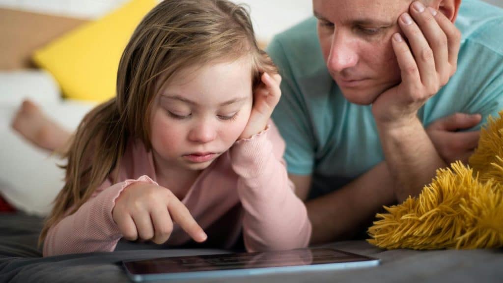 A girl pointing at a tablet as her father watches.