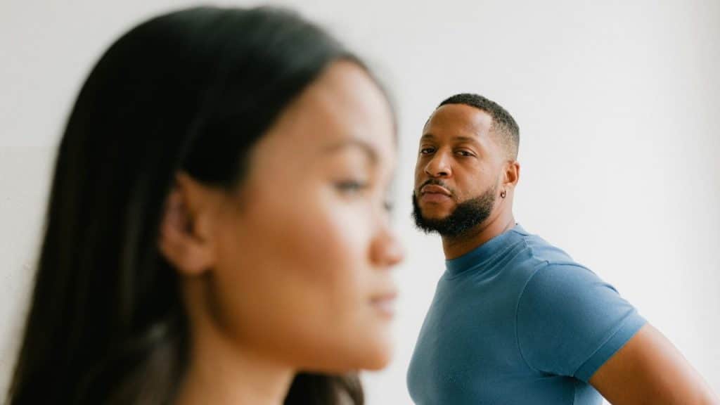 A blurred woman is in the foreground, while a man in a blue shirt looks over her shoulder.