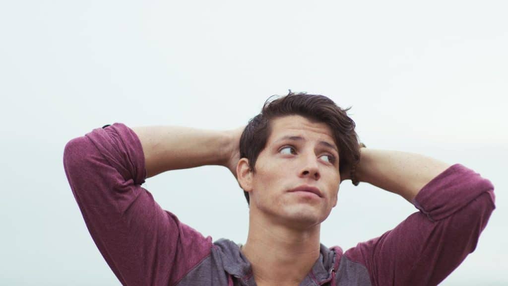 A young man with his hands behind his head, gazing upward.