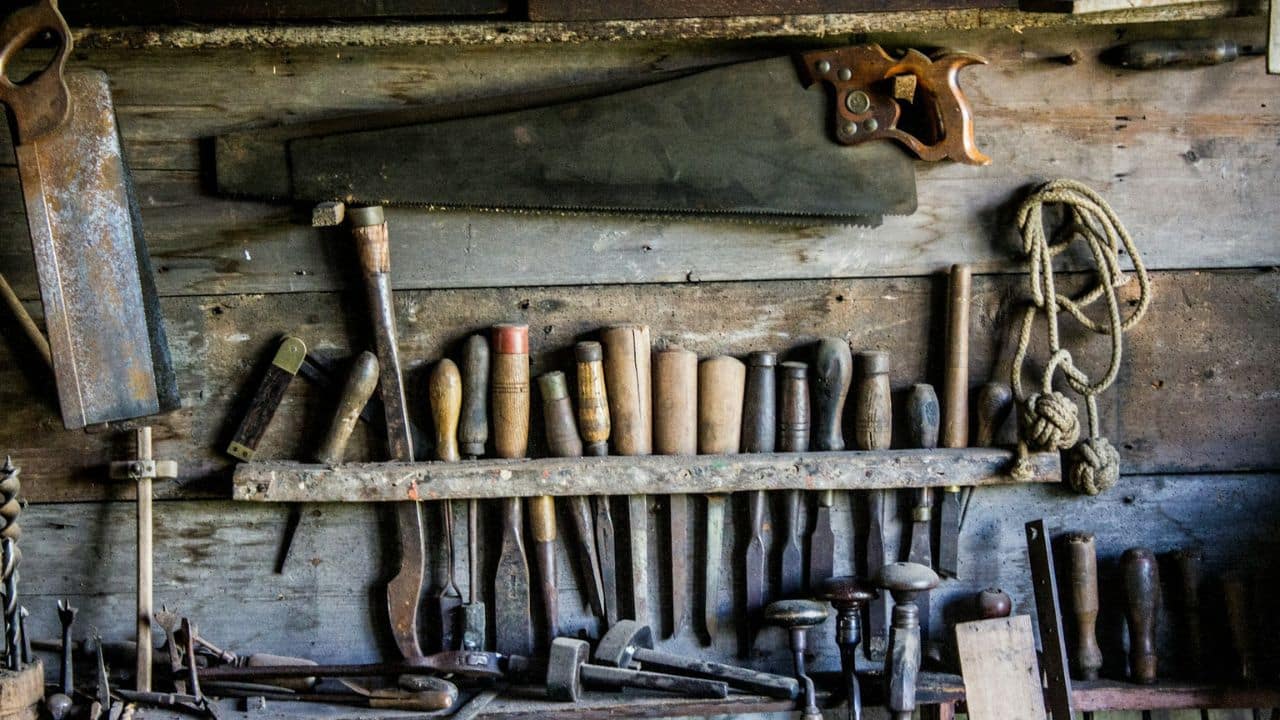 A wooden wall holds an assortment of old tools, including a large saw.