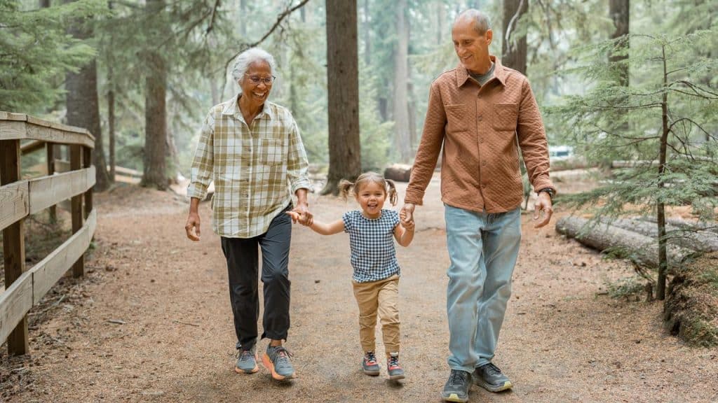 A senior couple walking hand‑in‑hand with their granddaughter on a forest trail.