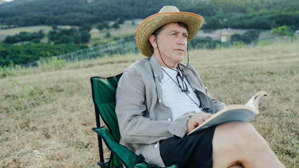 A man in a straw hat sits outdoors reading a book.