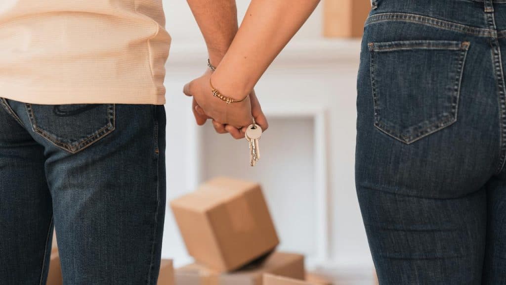 A couple holding house keys in front of stacked moving boxes.