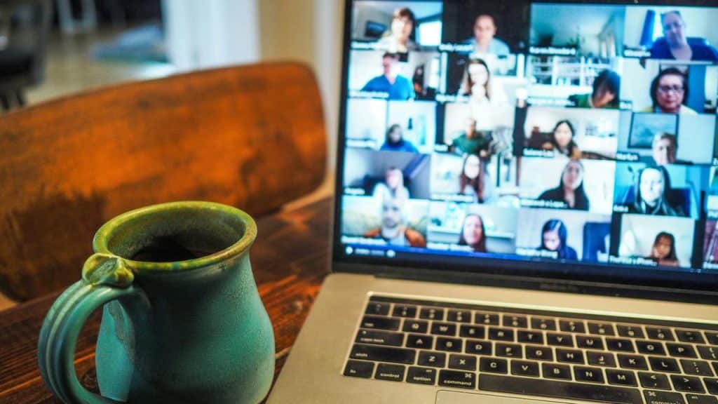 A green ceramic mug beside a laptop screen showing a grid of video call participants.