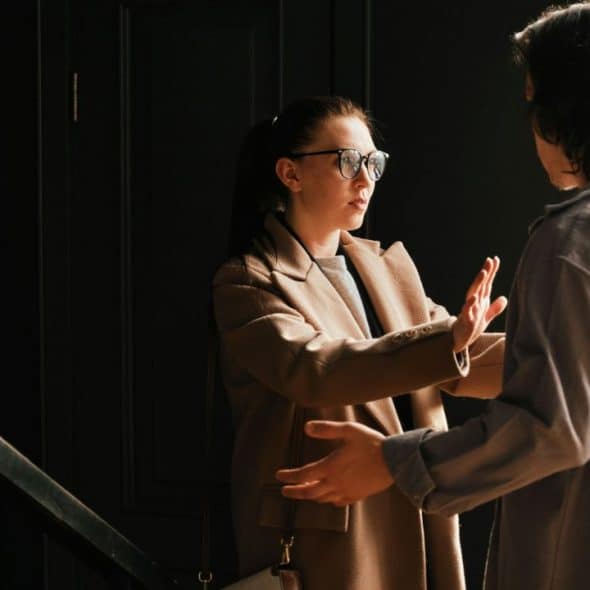 A woman in glasses holds up her hand towards a person with their back turned.