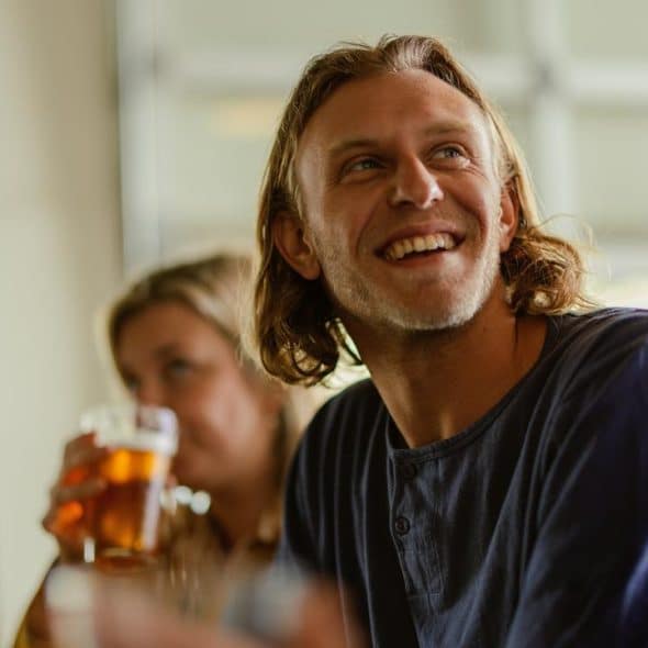 A smiling man holding a beer while chatting with friends.