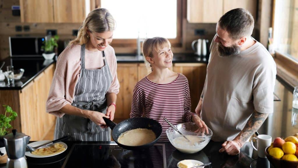 A family cooking pancakes together in a bright wooden kitchen.