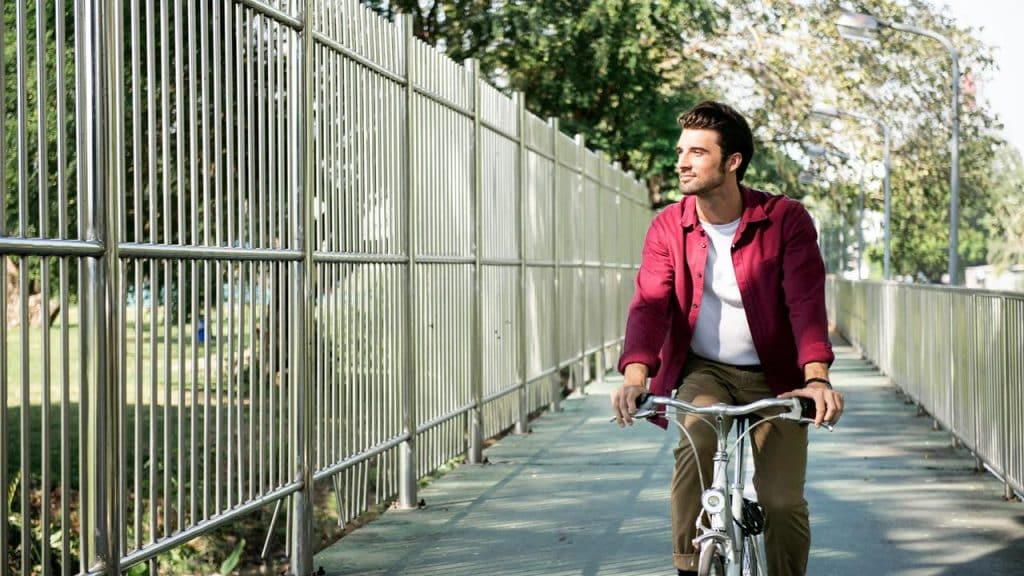 A man riding a bicycle along a fenced walkway.