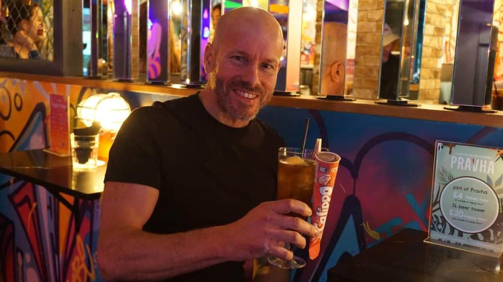 A smiling man holding a drink in a colorful bar.
