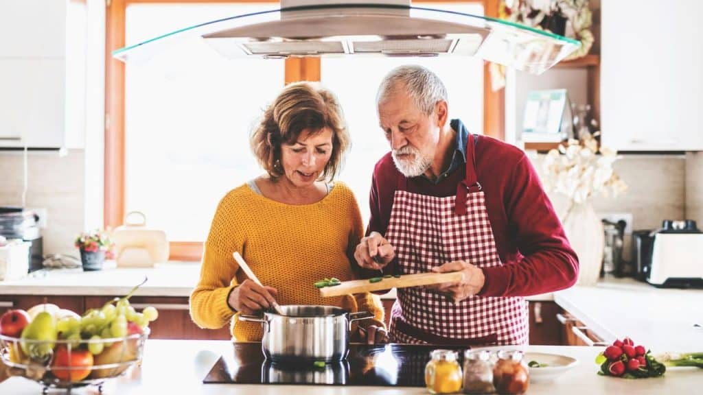 A cheerful senior couple is cooking together in a bright, modern kitchen.