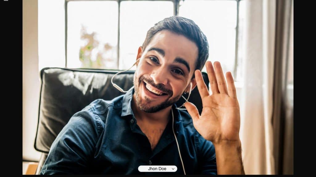 A smiling man wearing a headset and waving at the camera.