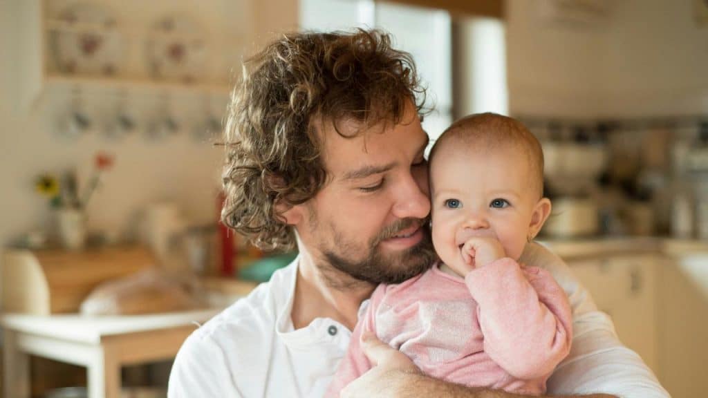 A man holding a baby who is sucking her finger.