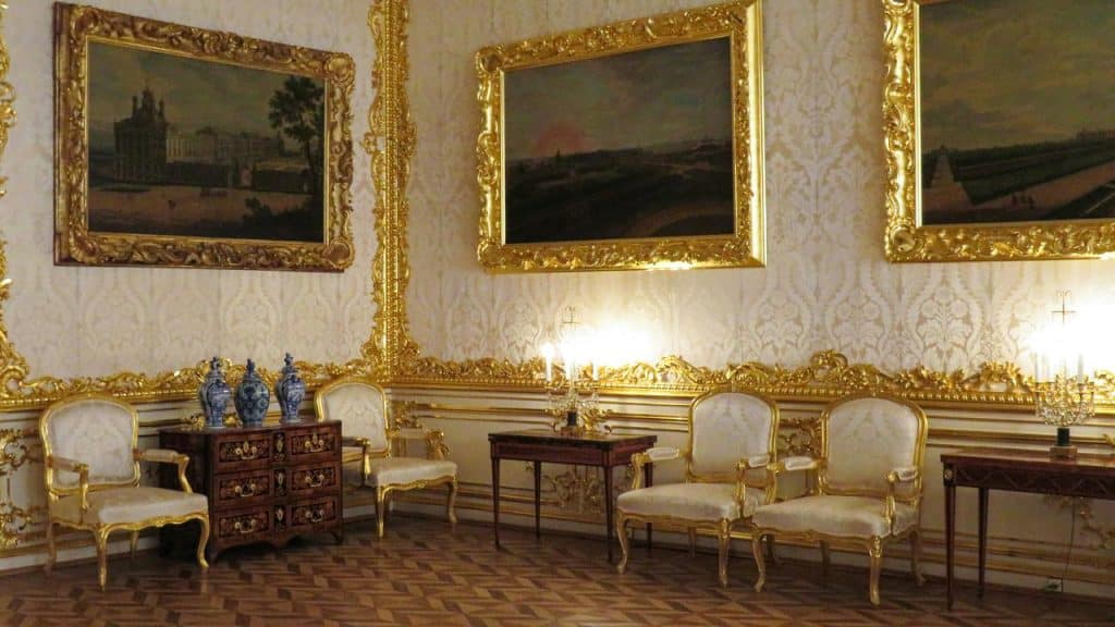 An ornate gilded home with gold-trimmed walls, antique chairs, and framed paintings.