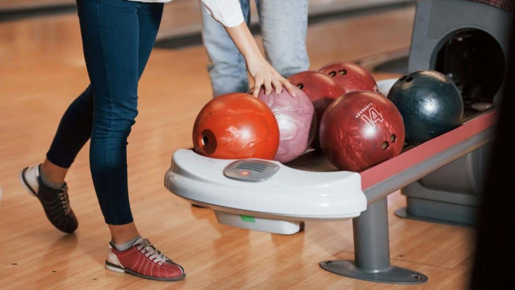 A bowler reaching for a ball on a bowling rack.