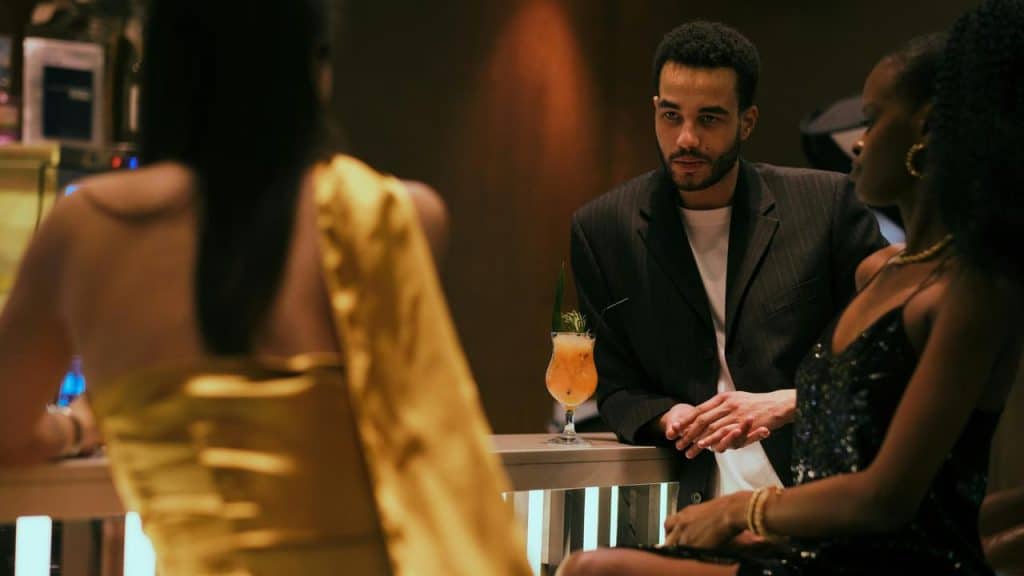 A suited man at a bar with two women and a cocktail.