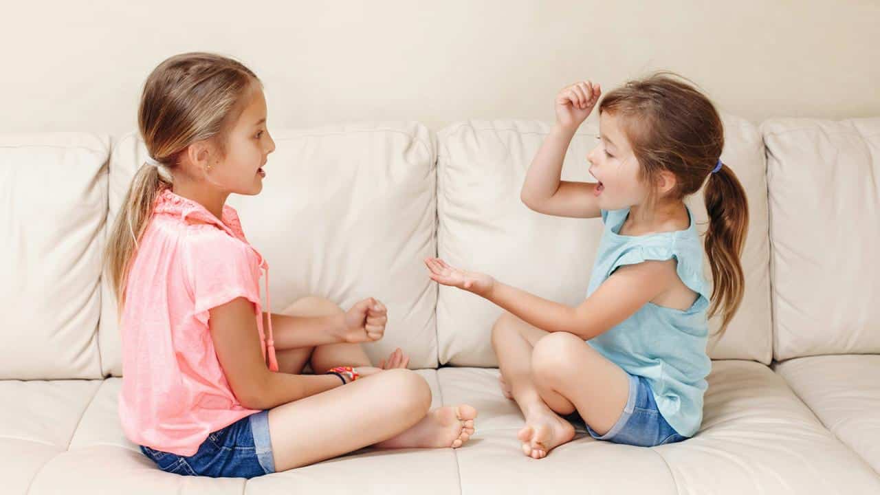 A pair of girls on a couch playing rock‑paper‑scissors.