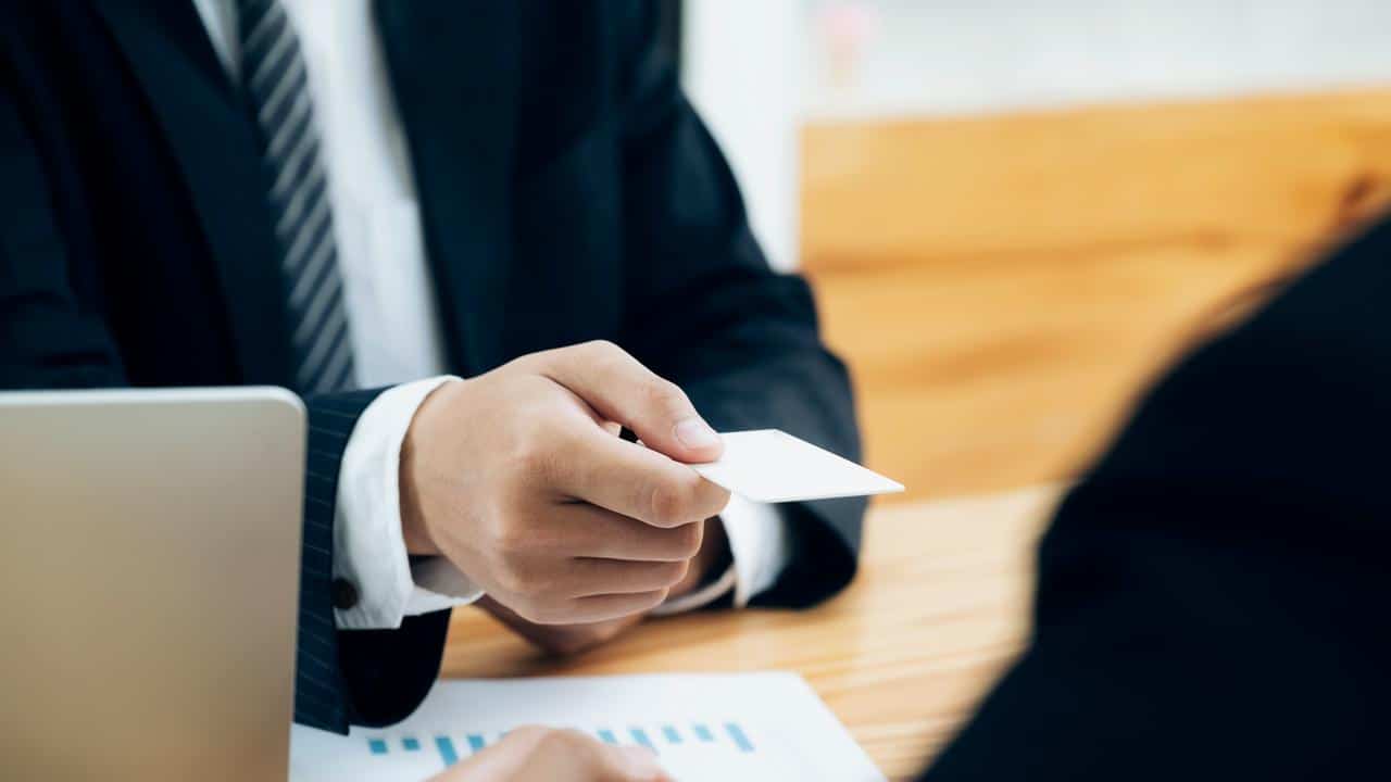 A suited person offering a business card.