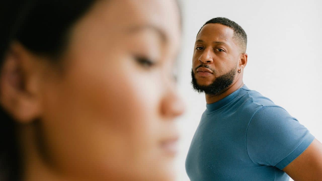 A blurry profile of a woman in the foreground with a man looking directly at the camera in the background.
