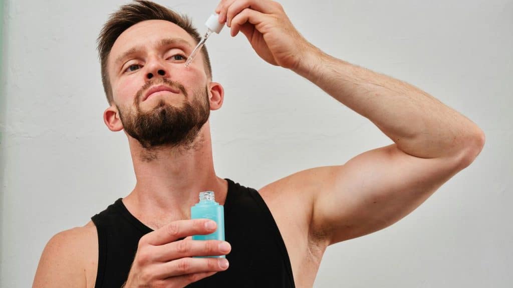 A man applying facial serum with a dropper from a blue bottle.