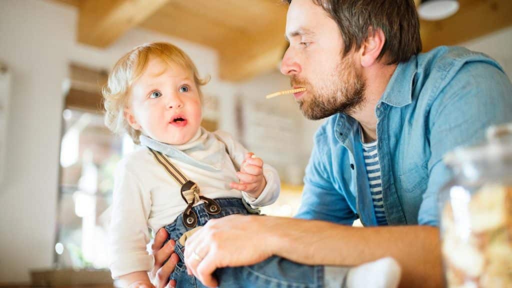A father and toddler sharing a snack in a kitchen.