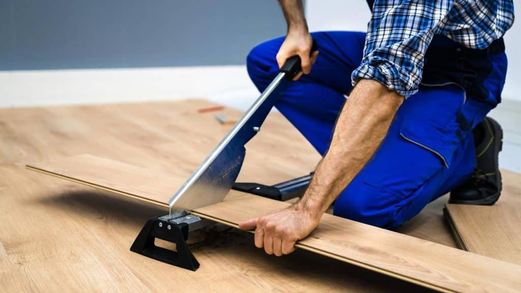 A person cutting a laminate floor plank with a manual plank cutter.