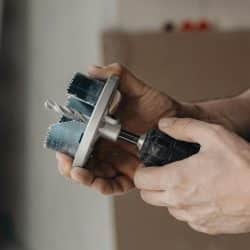A close-up of hands holding a power drill with a hole saw attachment.