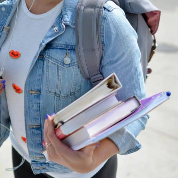A student holding a stack of textbooks while wearing a denim jacket.