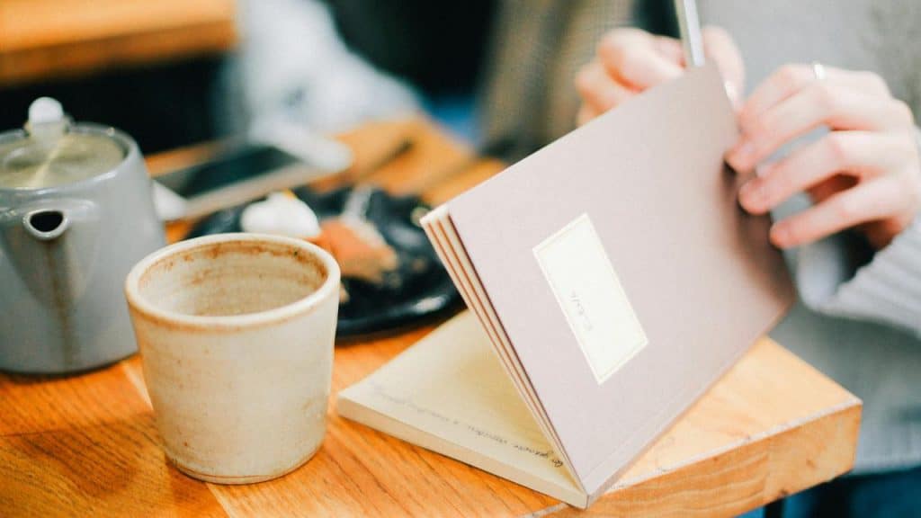 A person’s hand flipping through a notebook beside a ceramic mug.