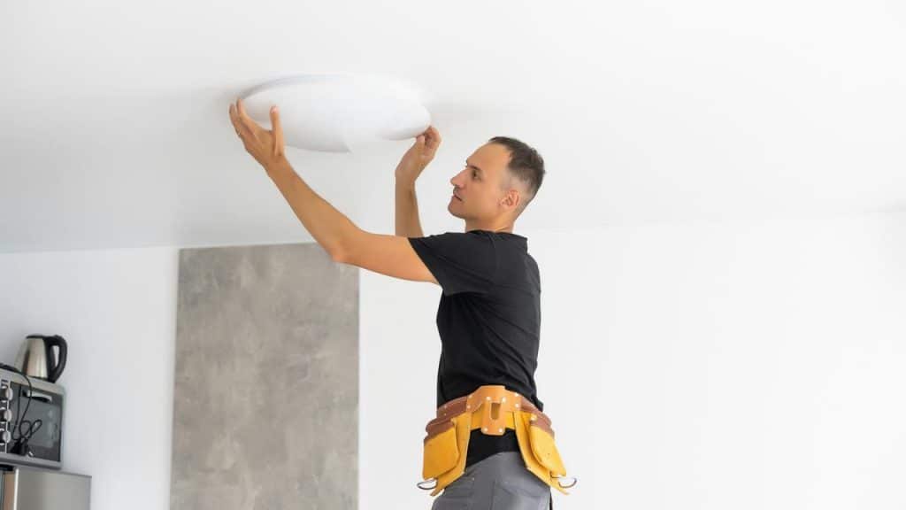 A man installing a ceiling light fixture.