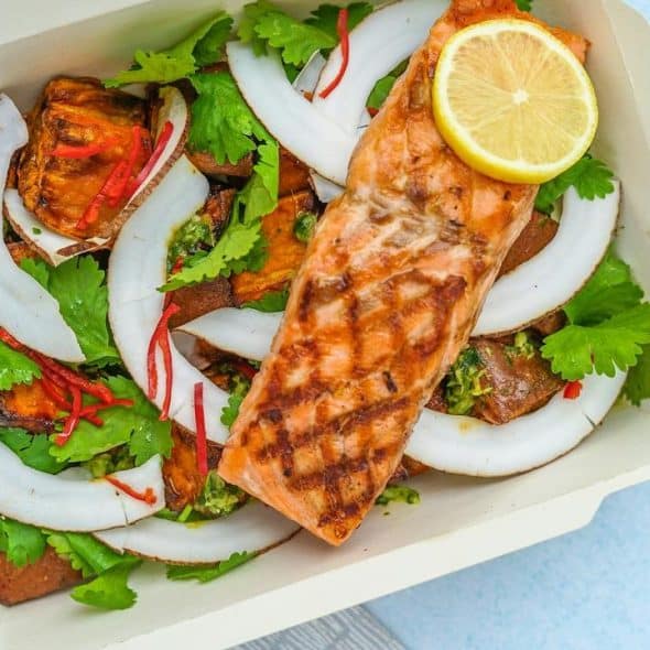 A takeout box with grilled salmon on a coconut‑potato salad.