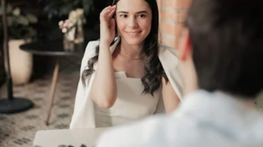 A woman brushing her hair behind her ear while looking at a man