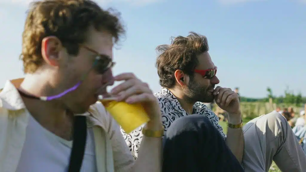 A pair of men outdoors, one sipping a drink.