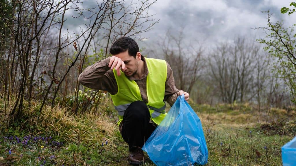 A man in a reflective vest picking up litter outdoors.