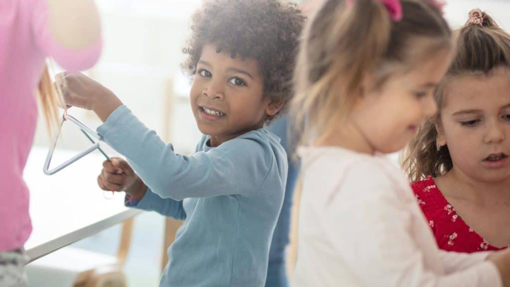 A boy playing a metal triangle instrument alongside other children.