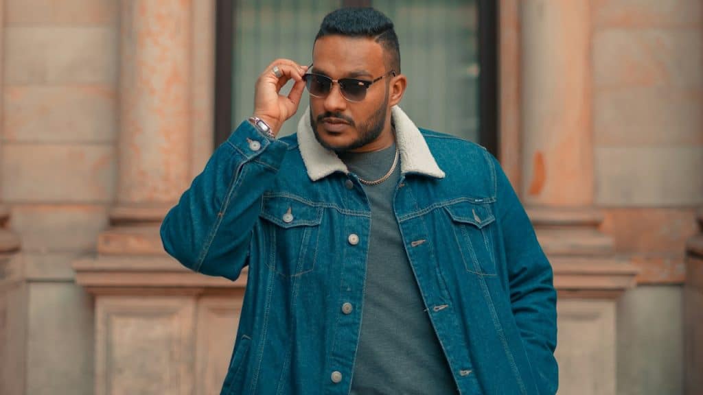 A man wearing a glasses and jacket standing outdoors.