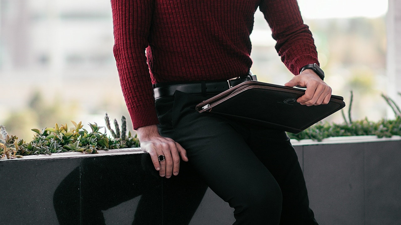 A man wearing a sweater over tailored pants.