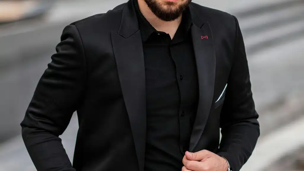 A bearded man wearing a black colored shirt and coat.