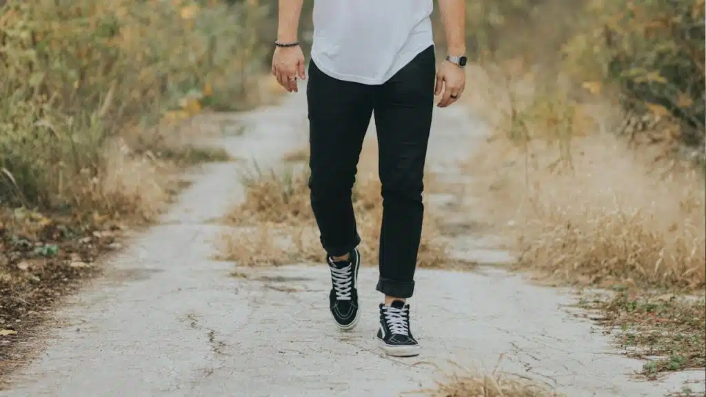A man wearing jeans and sneakers walking on a path. 