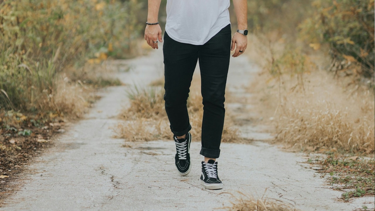 A man wearing jeans and sneakers walking on a path.