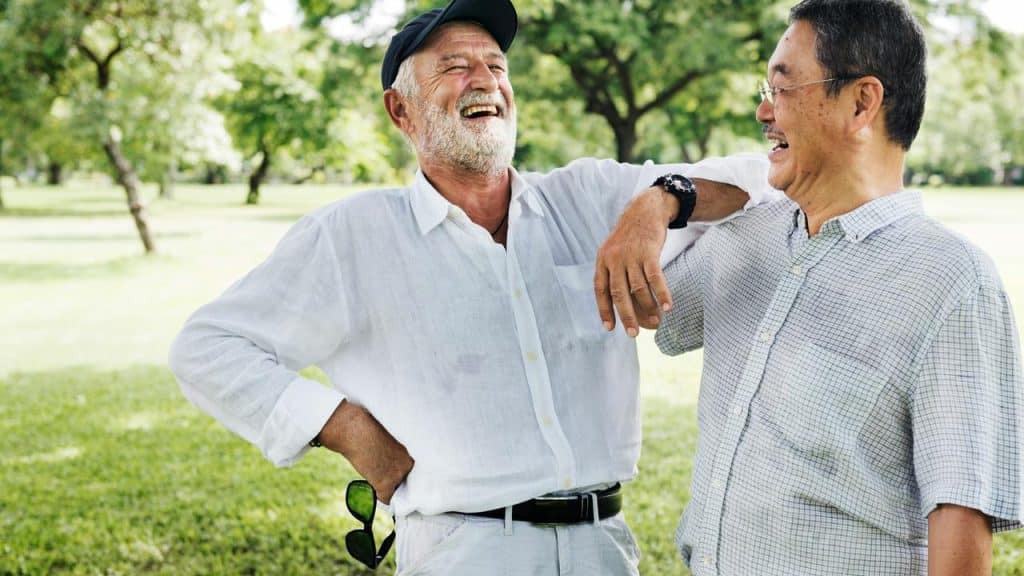 An older man and his friend laughing together in a park.