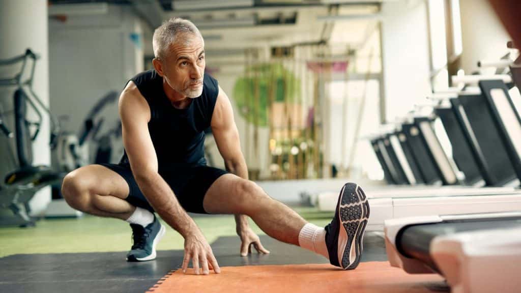 A man stretches his leg on a gym floor.