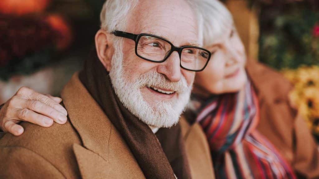 A smiling elderly couple dressed warmly outdoors.