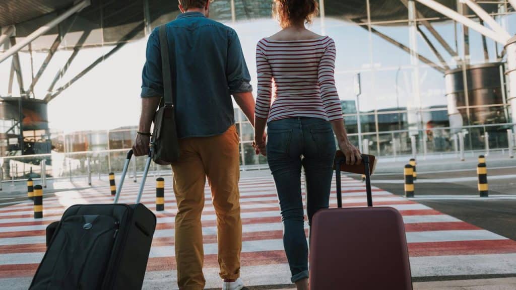A couple walking toward an airport terminal with suitcases.